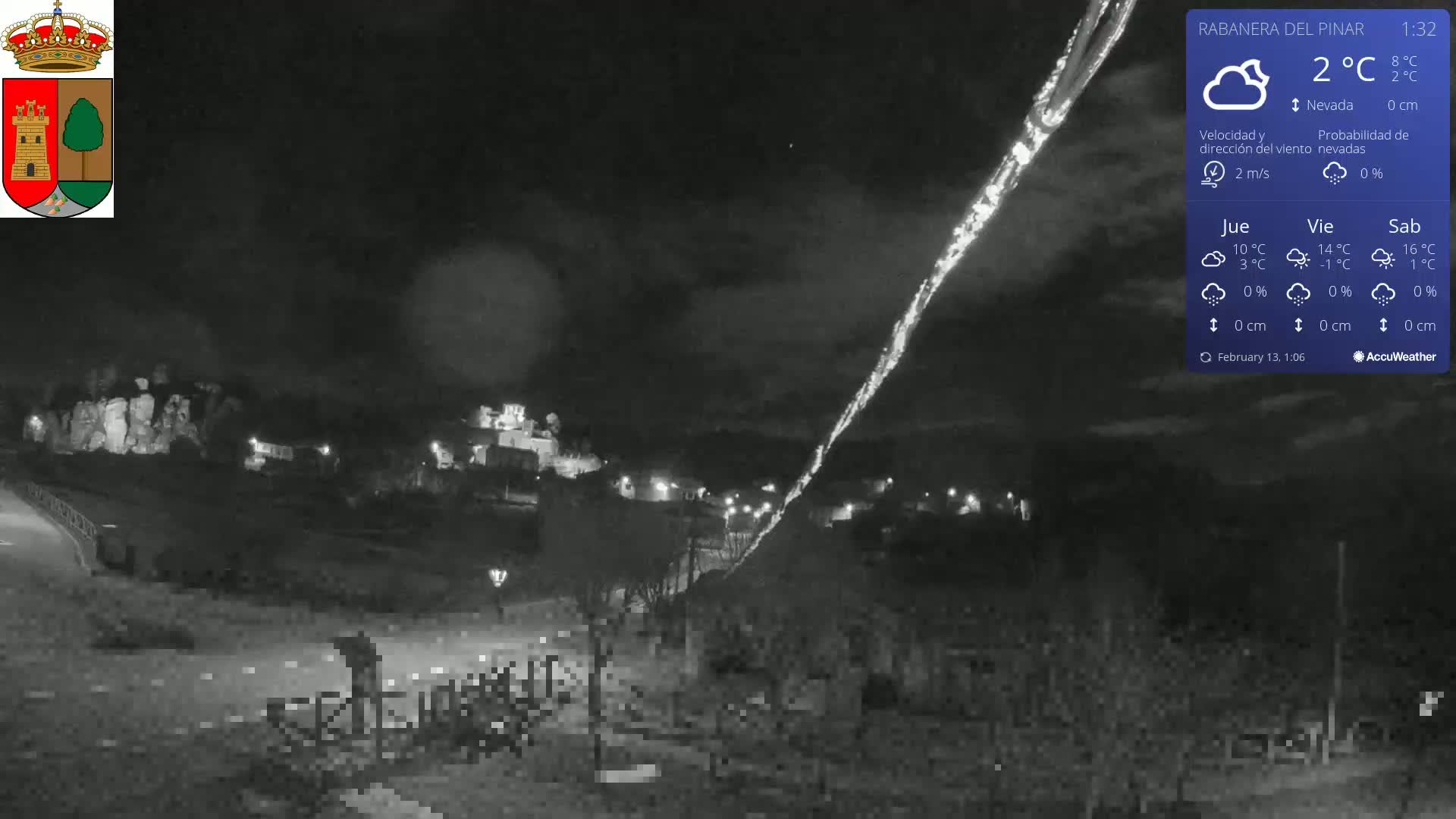 A nighttime, low-light view of a town with a long, bright streak across the dark sky, possibly a meteor, under mostly clear skies and a temperature of 2°C.