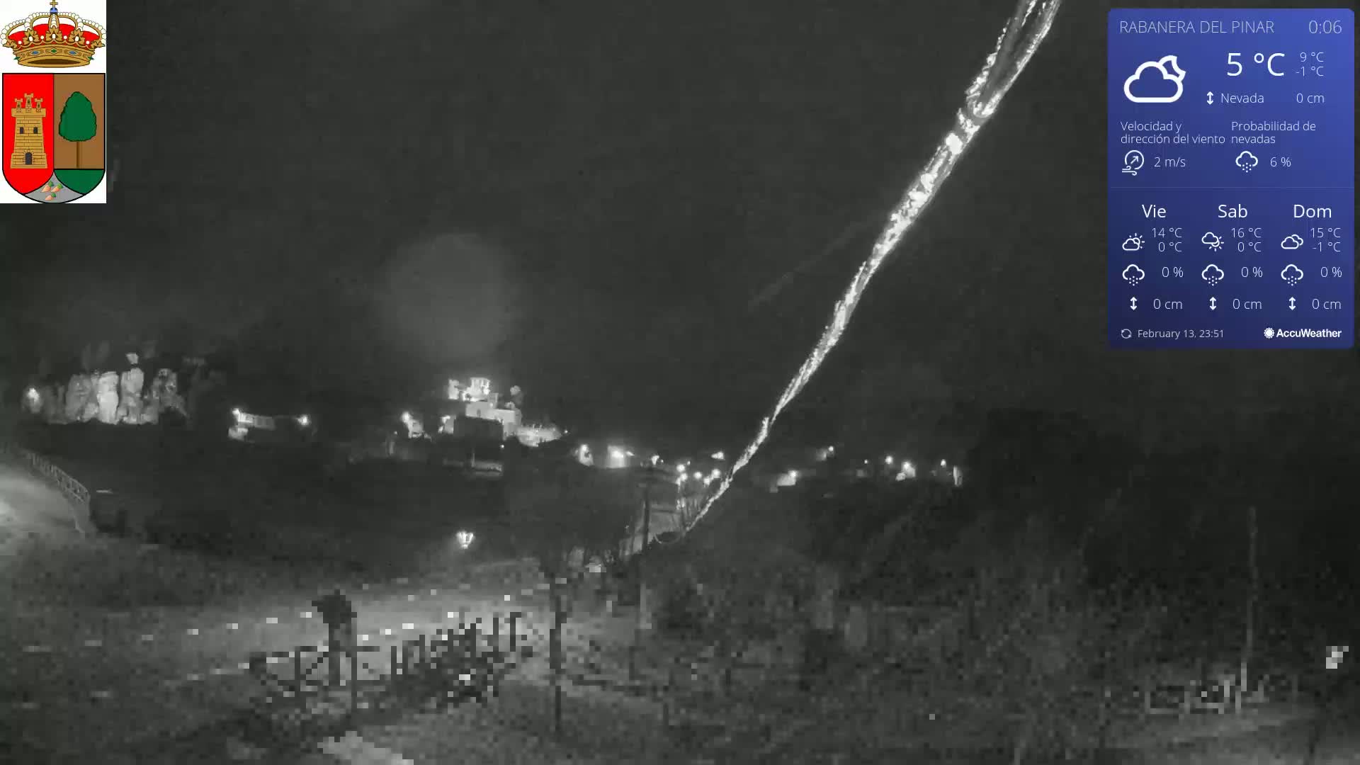 A nighttime, snowy scene shows a village illuminated by lights under a cloudy sky.