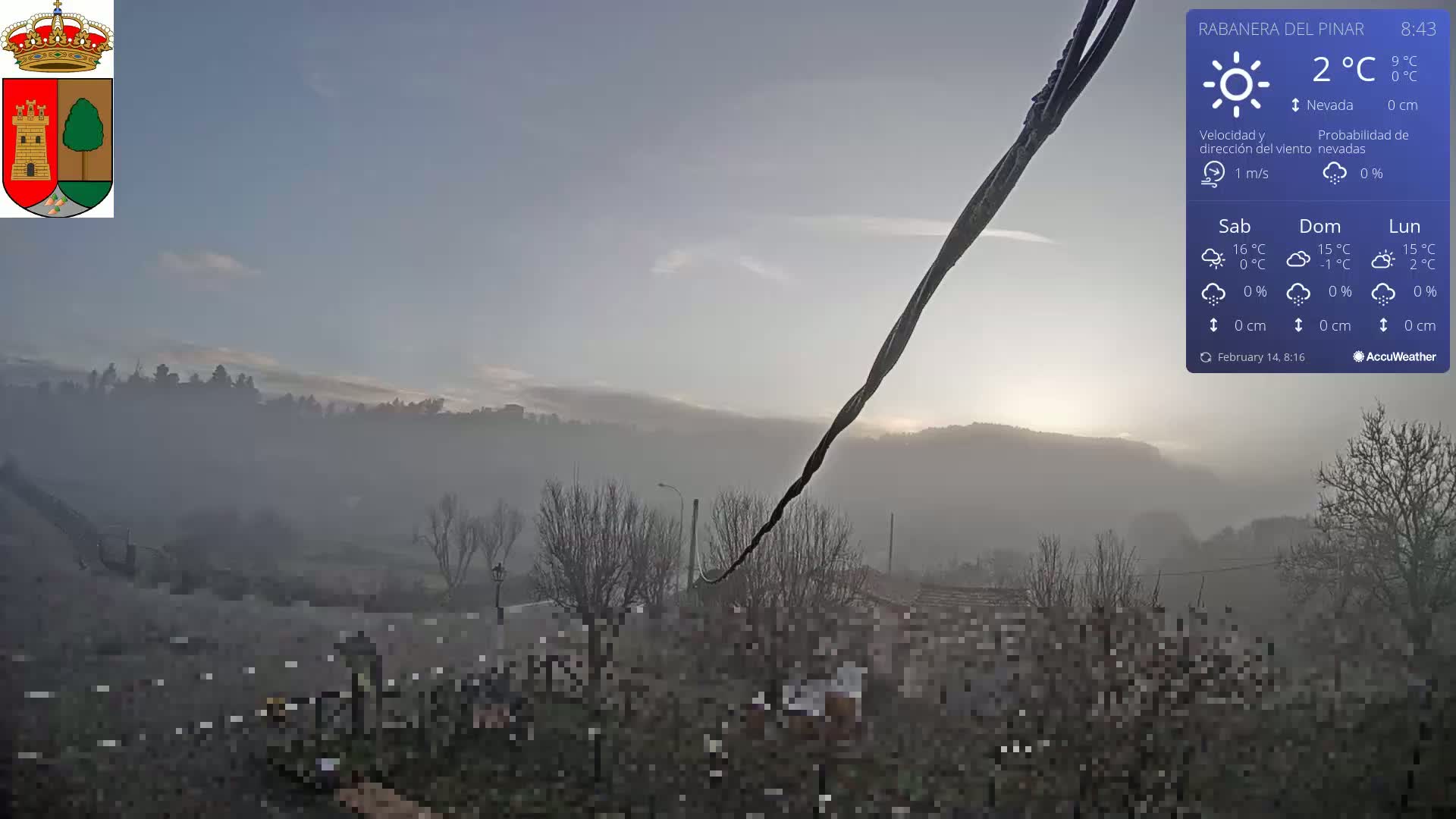 A hazy, foggy sunrise illuminates a landscape of bare winter trees and distant hills under a pale sky.