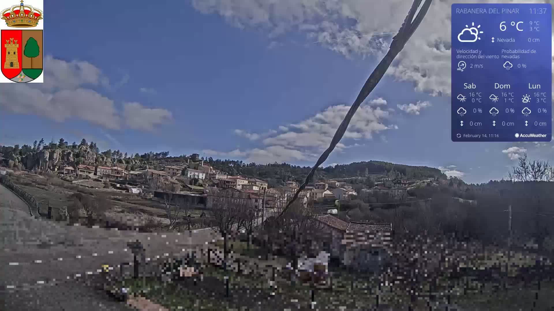 A small village nestled in a hillside is visible under a partly cloudy blue sky.