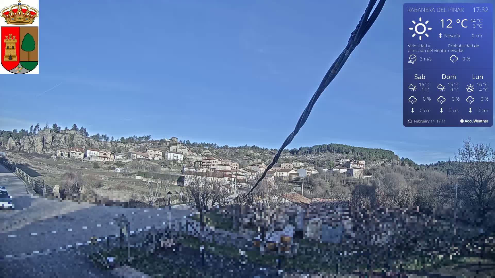 A small village nestled in a hilly landscape under a clear blue sky on a sunny 12°C day.