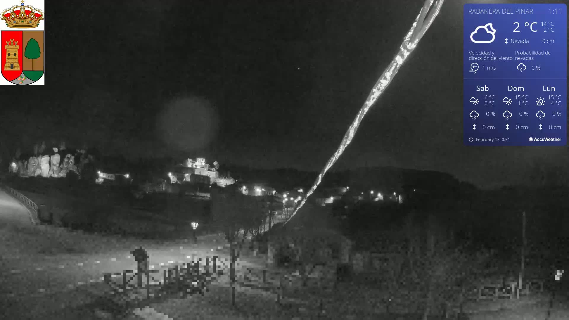 A nighttime, low-light view of a town illuminated with a bright streak of light across the sky under clear, snowy conditions, with a temperature of 2°C.