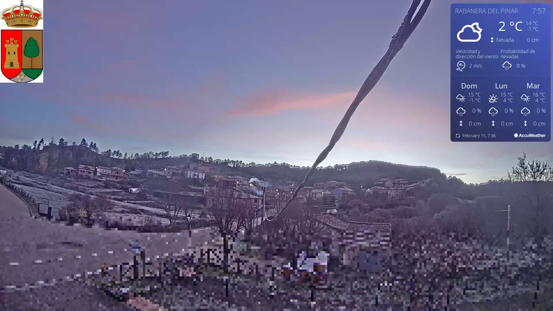 A small village nestled in a hillside is visible under a twilight sky with a light pink hue and cloudy, 2°C weather.