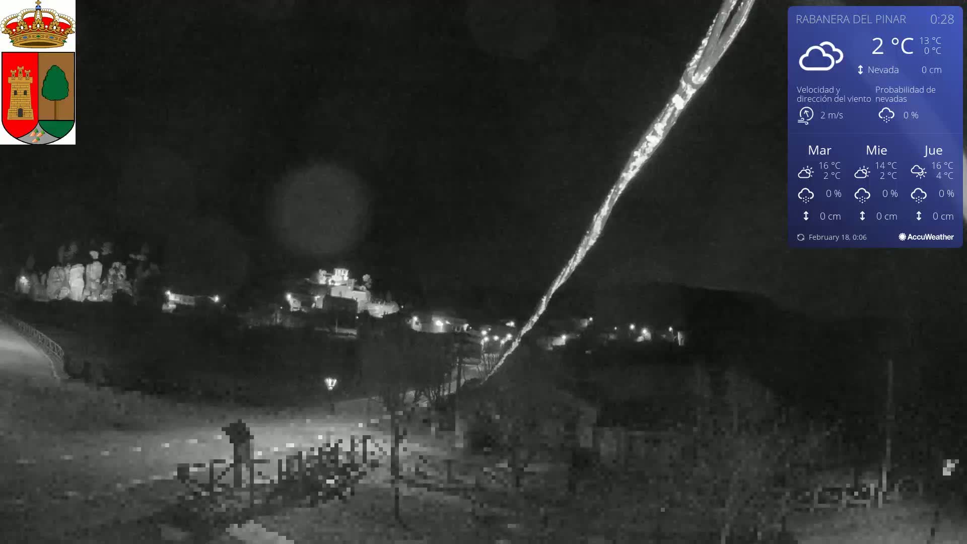 A nighttime, low-resolution view of a small town with a bright streak of light across the dark sky, under mostly clear skies and a temperature of 2°C.