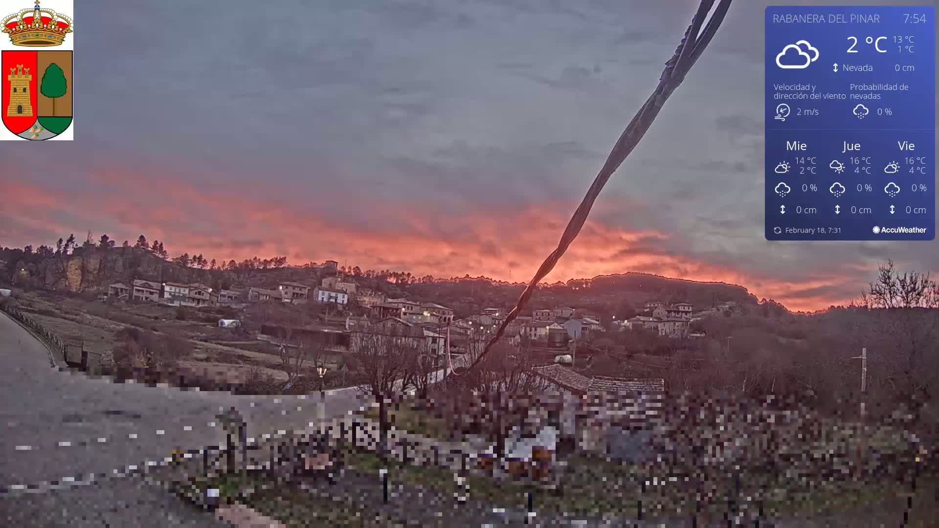 A village nestled in a hillside is bathed in the warm glow of a pinkish-red sunset under a mostly clear sky.