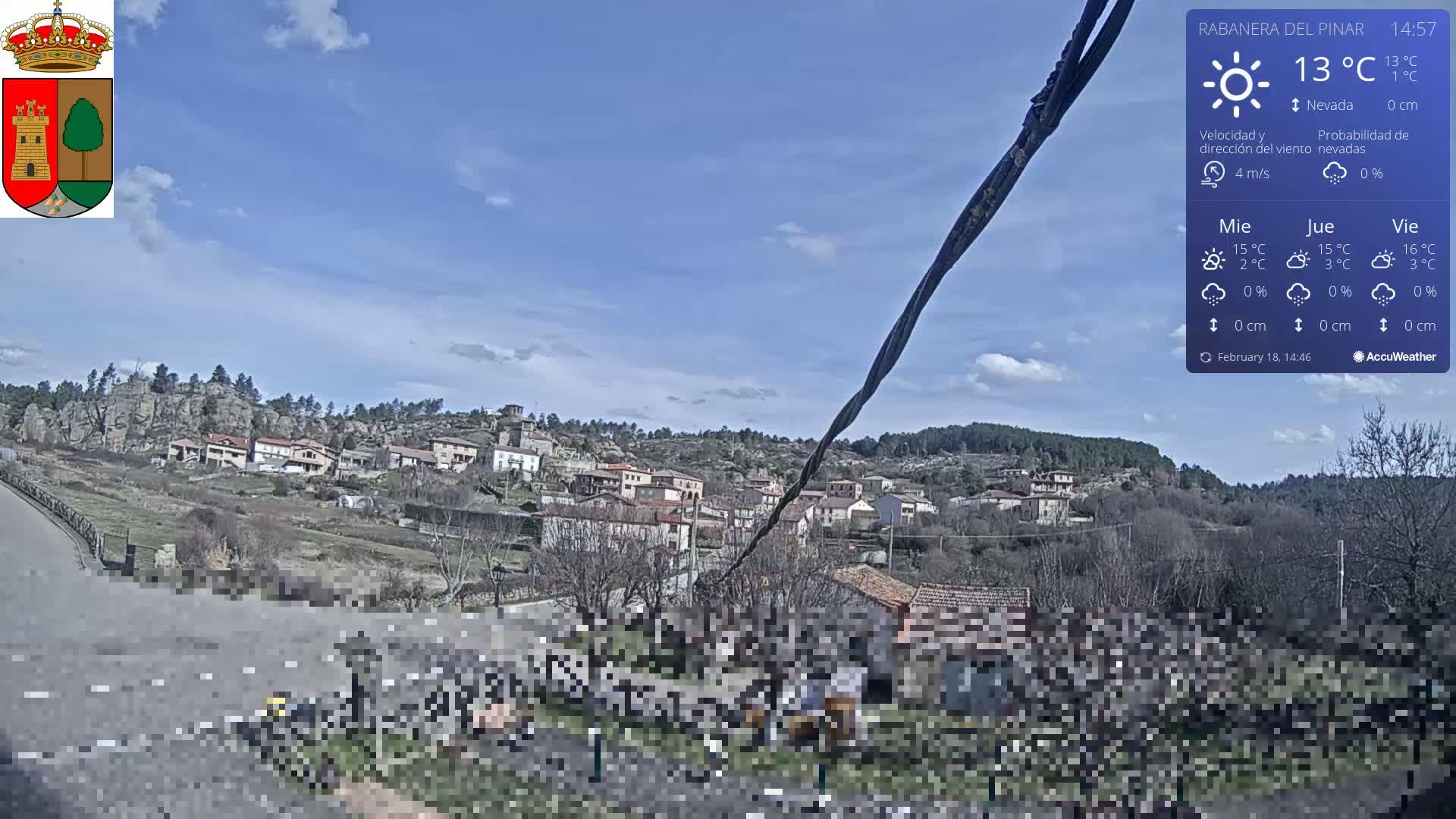A small village nestled on a hillside under a mostly clear, sunny sky is viewed from a slightly elevated vantage point.
