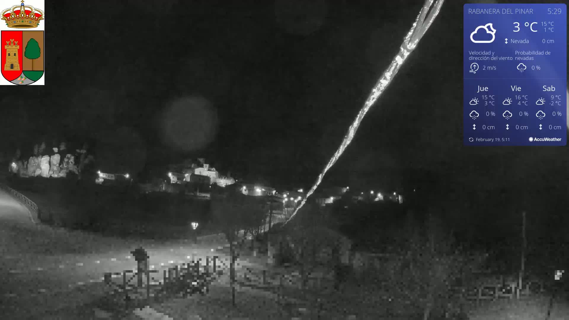 A nighttime, snowy scene shows a small town illuminated with lights, with a bright streak in the sky.