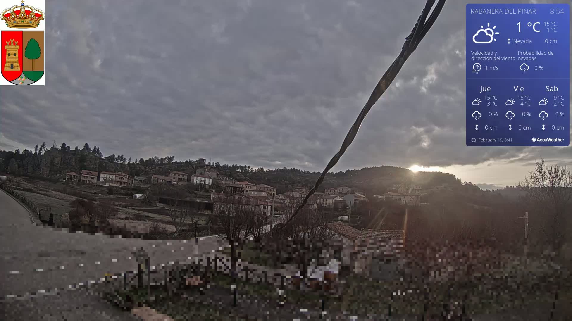 A partly cloudy sunset illuminates a small village nestled on a hillside, with a light breeze.