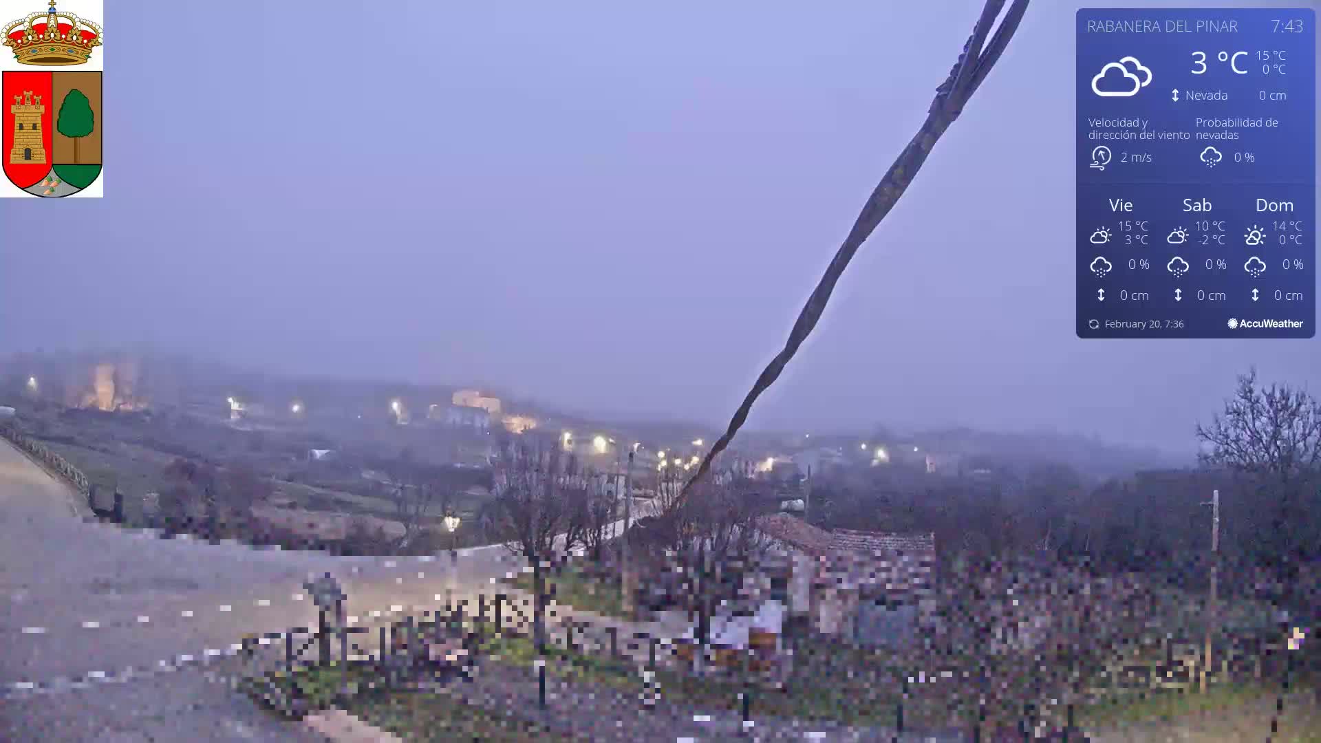 A hazy, overcast nighttime view of a rural village with dimly lit buildings and a road winding through the landscape, under a 3°C temperature.