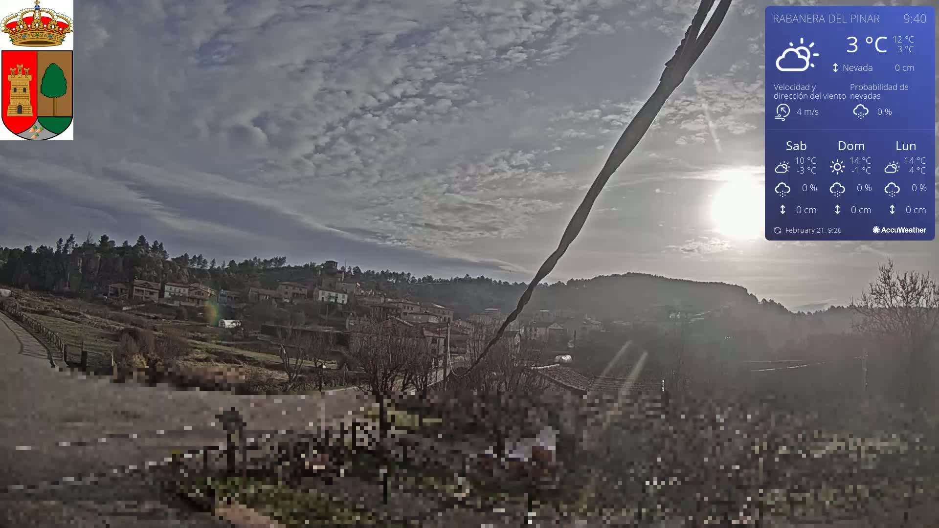A partly sunny view of a small town nestled in a hillside, under a mostly cloudy sky with a 3°C temperature.