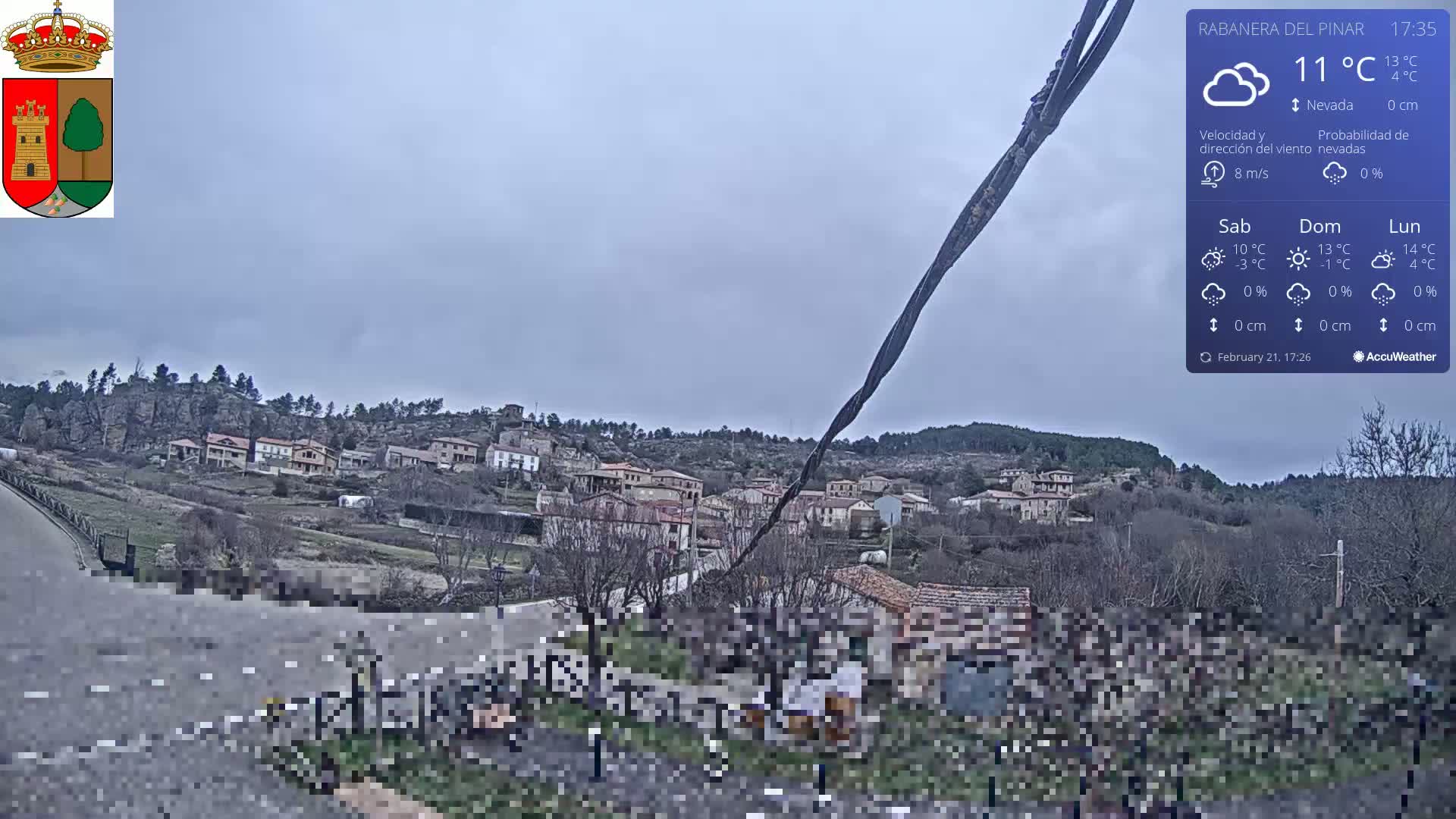 A small village nestled in a hillside, viewed from a roadside on an overcast day.
