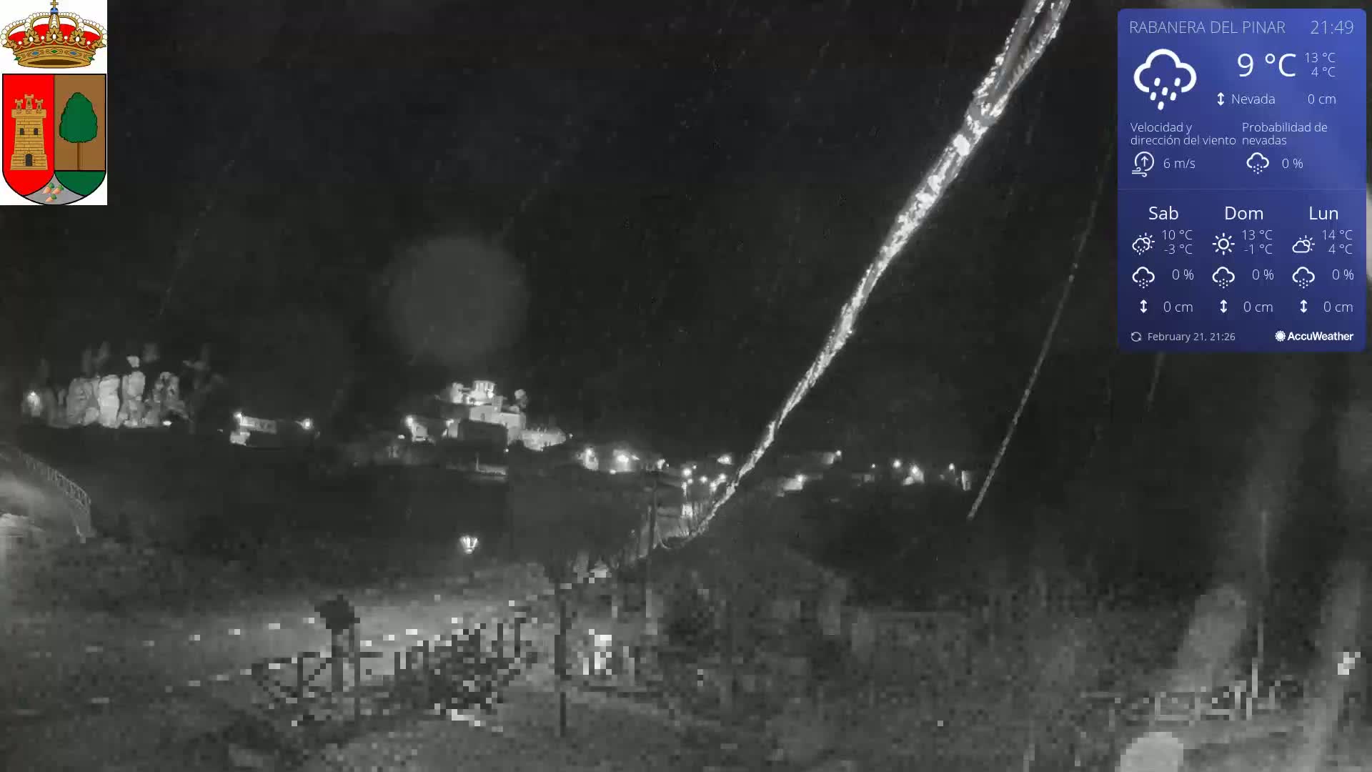 A nighttime, snowy scene shows a small town illuminated by scattered lights under a dark sky.