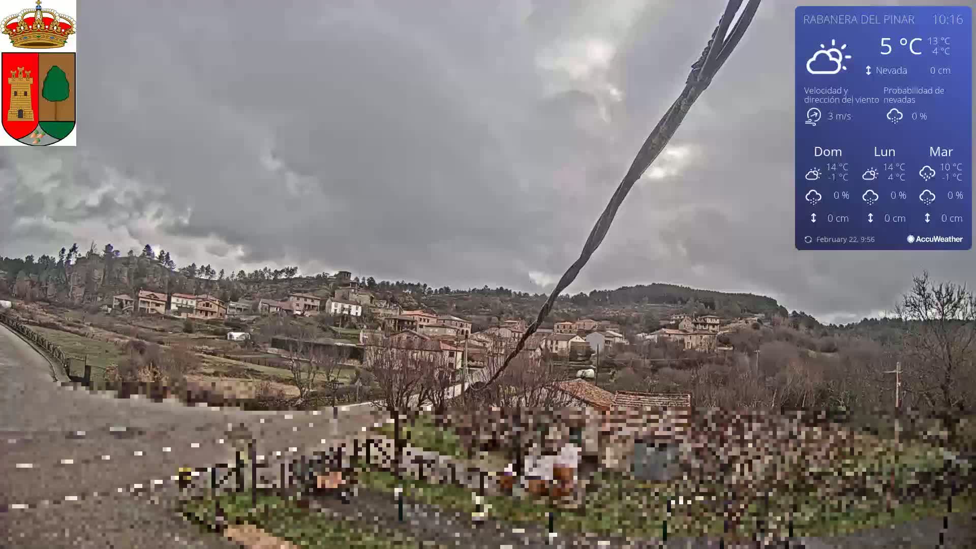 A small village nestled in a hillside under an overcast sky is viewed from a roadside vantage point.