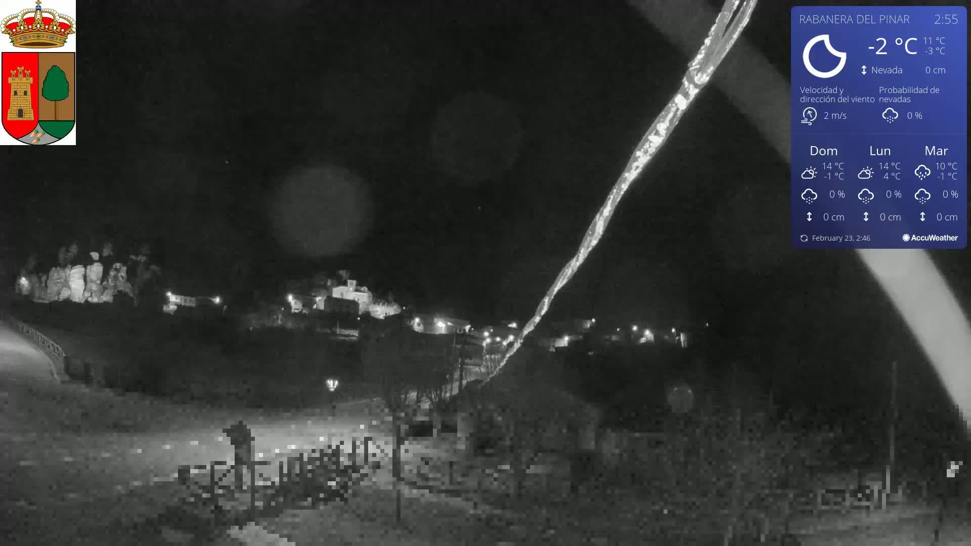 A nighttime, snowy scene shows a small town illuminated under a dark sky with a bright streak in the sky, possibly a light trail.