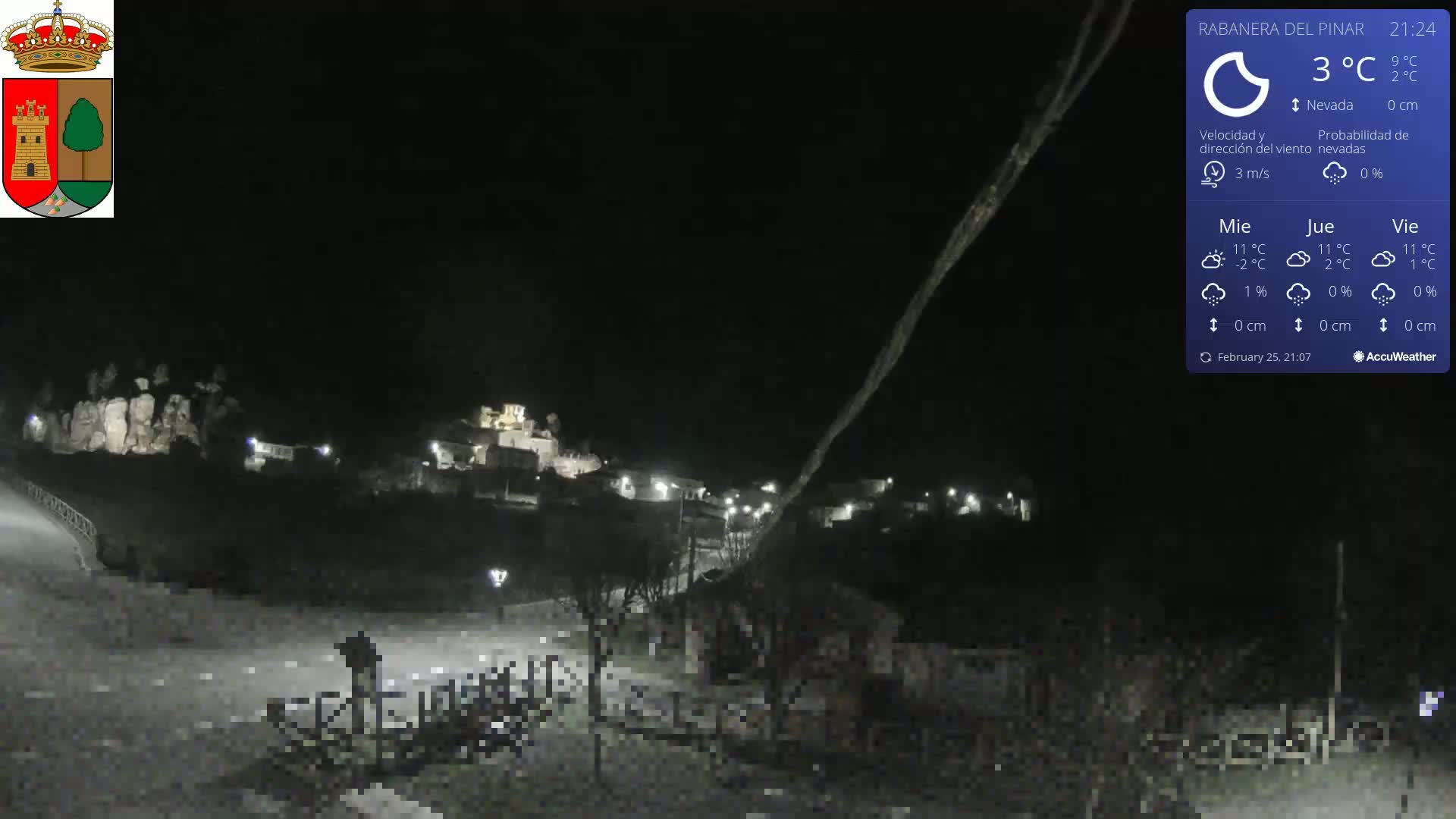 A nighttime view of a small town illuminated by streetlights, under a dark sky with light snowfall.