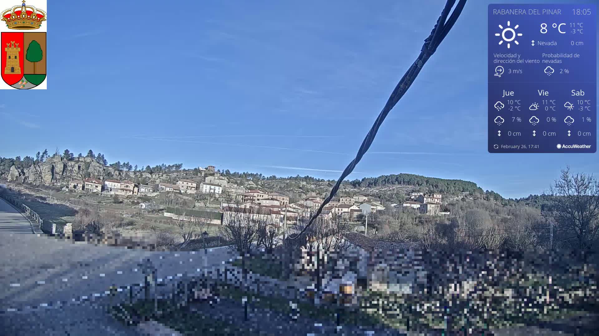 A small village nestled on a hillside under a clear blue sky, with a road and bridge visible in the foreground.
