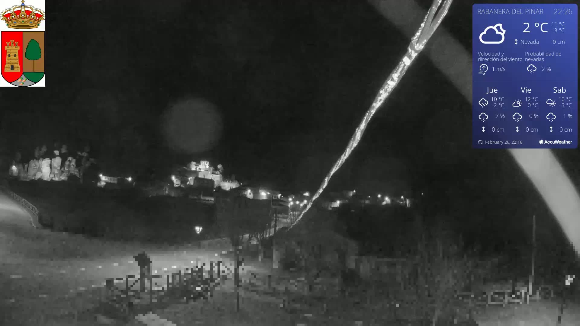 A nighttime, snowy scene shows a small town illuminated under a dark sky with a faint streak of light in the upper right.