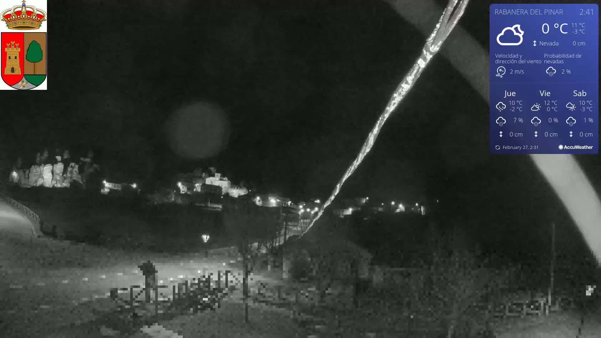 A nighttime, snow-free scene shows a small town illuminated by lights, with a long, bright streak in the sky under a dark, clear sky.