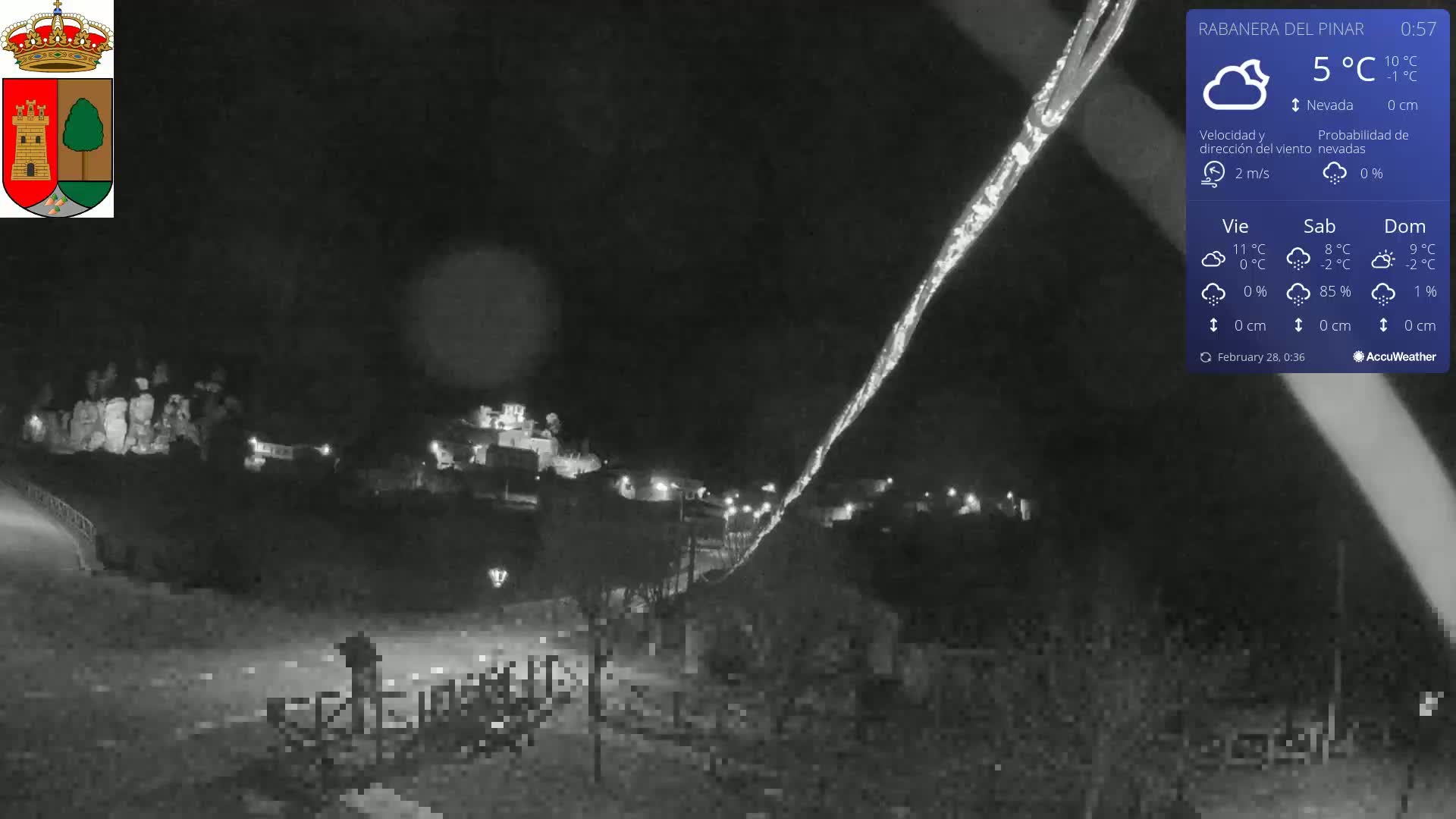 A nighttime, snowy scene shows a small town with dim lights under a dark sky, illuminated by a bright streak of light in the upper right corner.