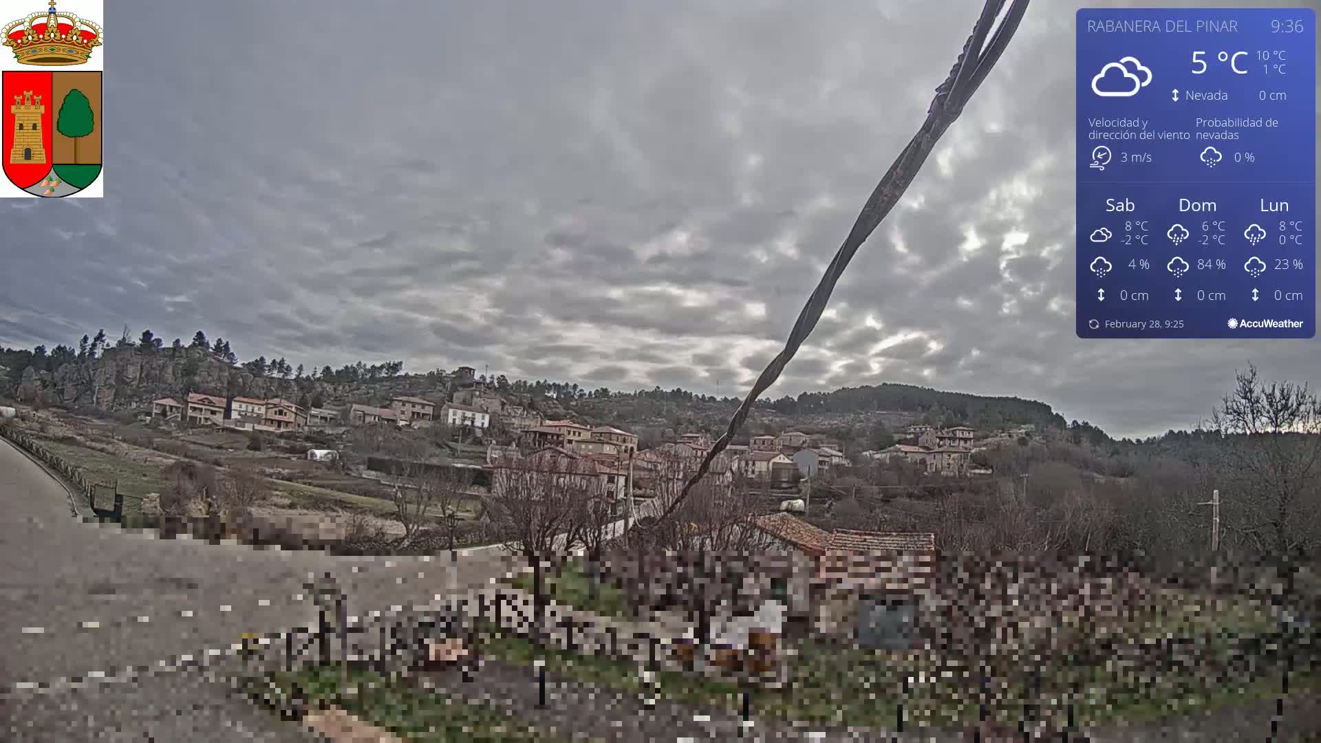 A small village nestled in a hillside under a cloudy sky is viewed from a slightly elevated position.