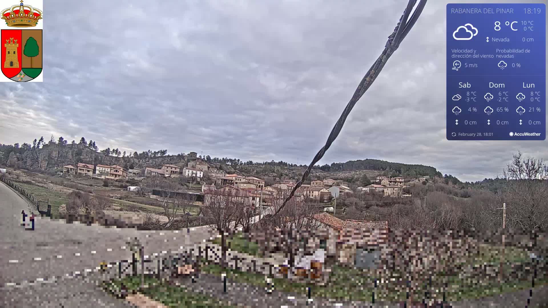 A small village nestled in a hillside, under a cloudy sky, is viewed from a slightly elevated perspective.