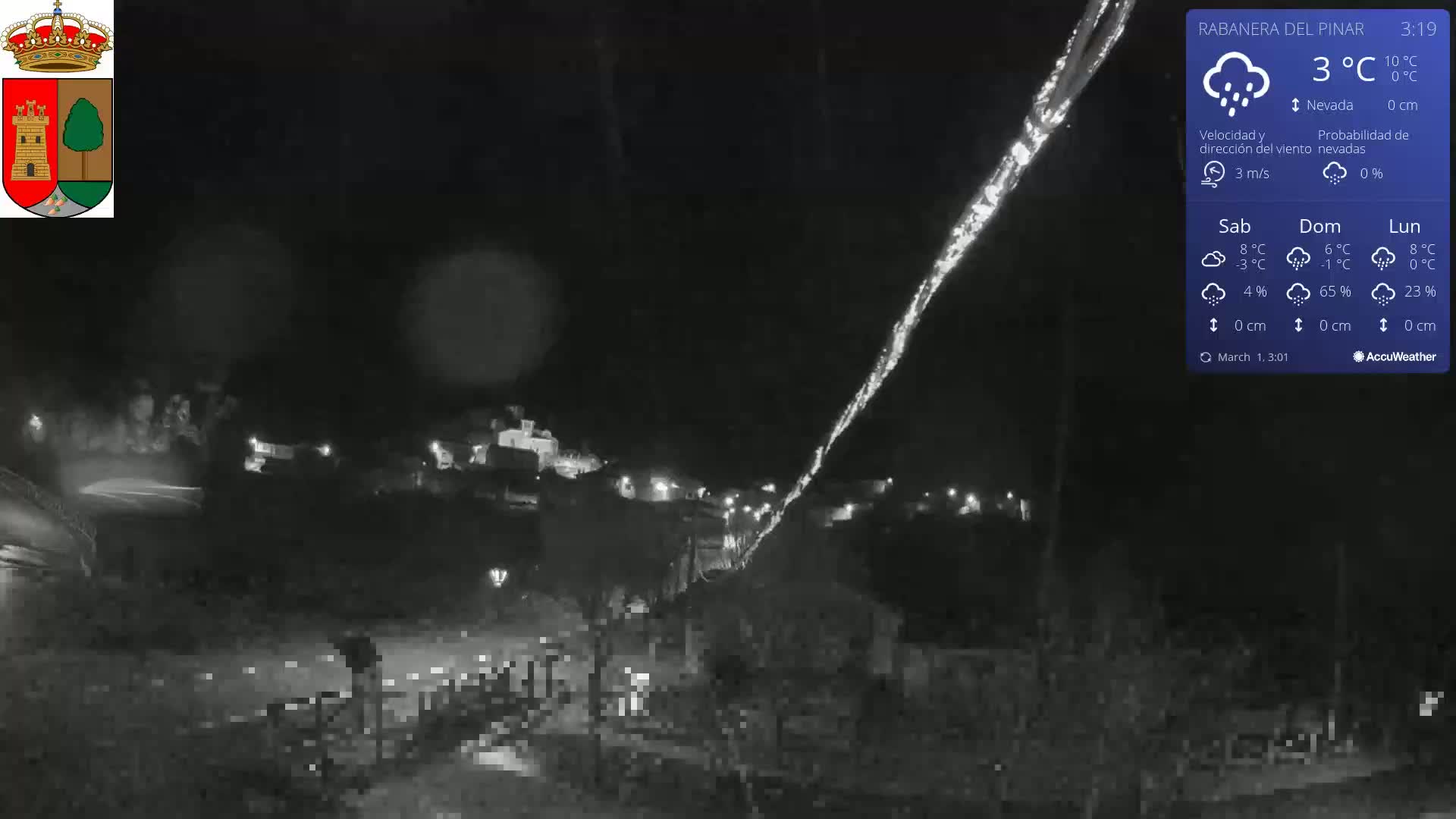A nighttime view of a small town illuminated by scattered lights, under a dark, rainy sky.