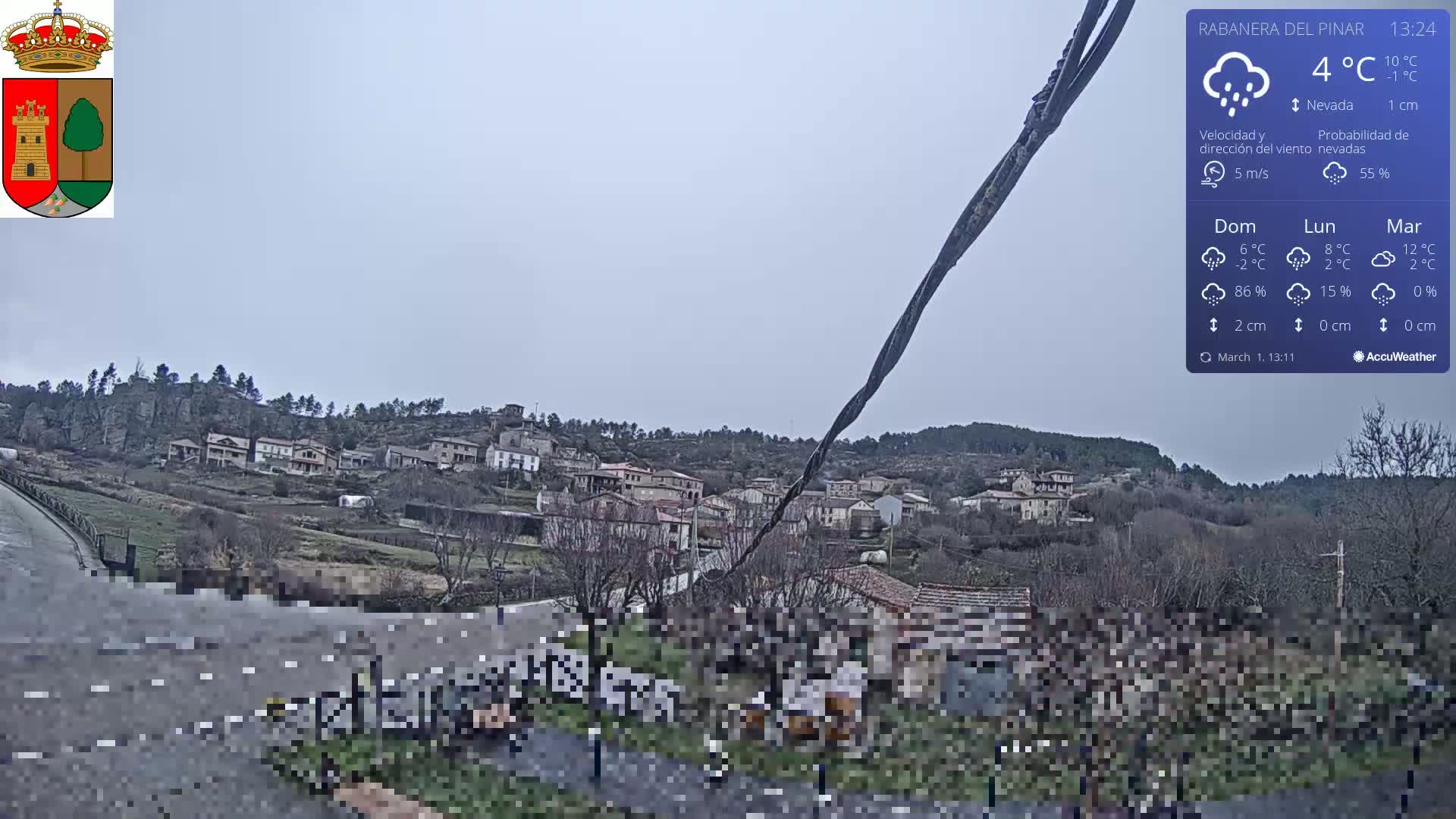 A small village nestled in a hillside is lightly dusted with snow under an overcast sky.