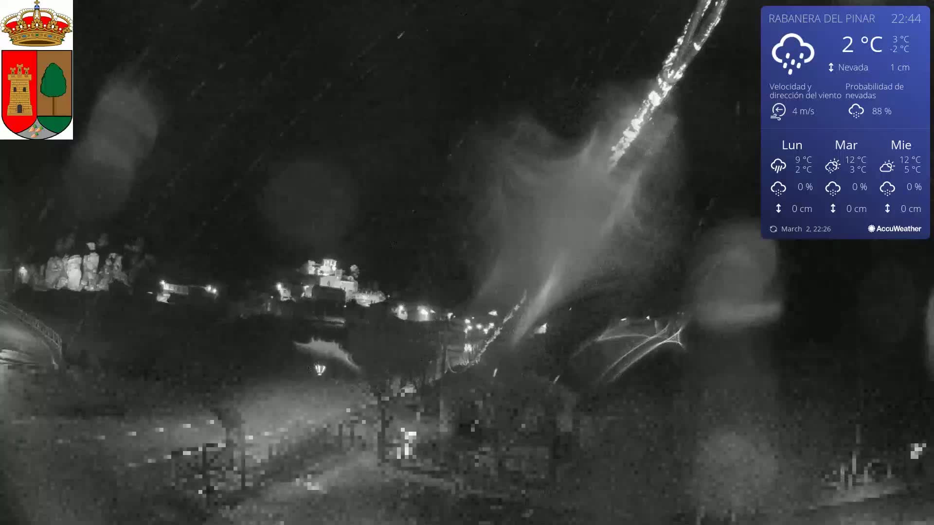 A nighttime, snowy scene shows a town illuminated by lights under heavy snowfall.