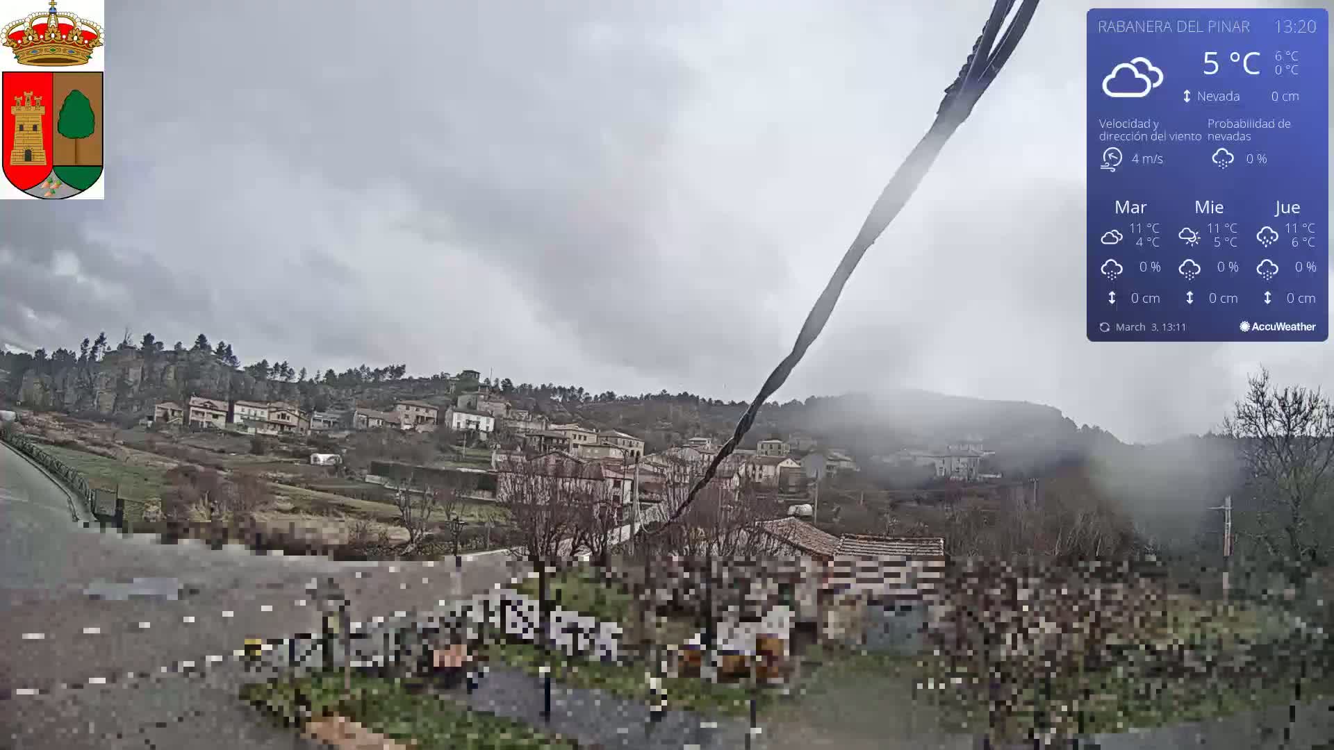 A cloudy, overcast day reveals a small village nestled in a hillside valley, with a wiper blade in the foreground.