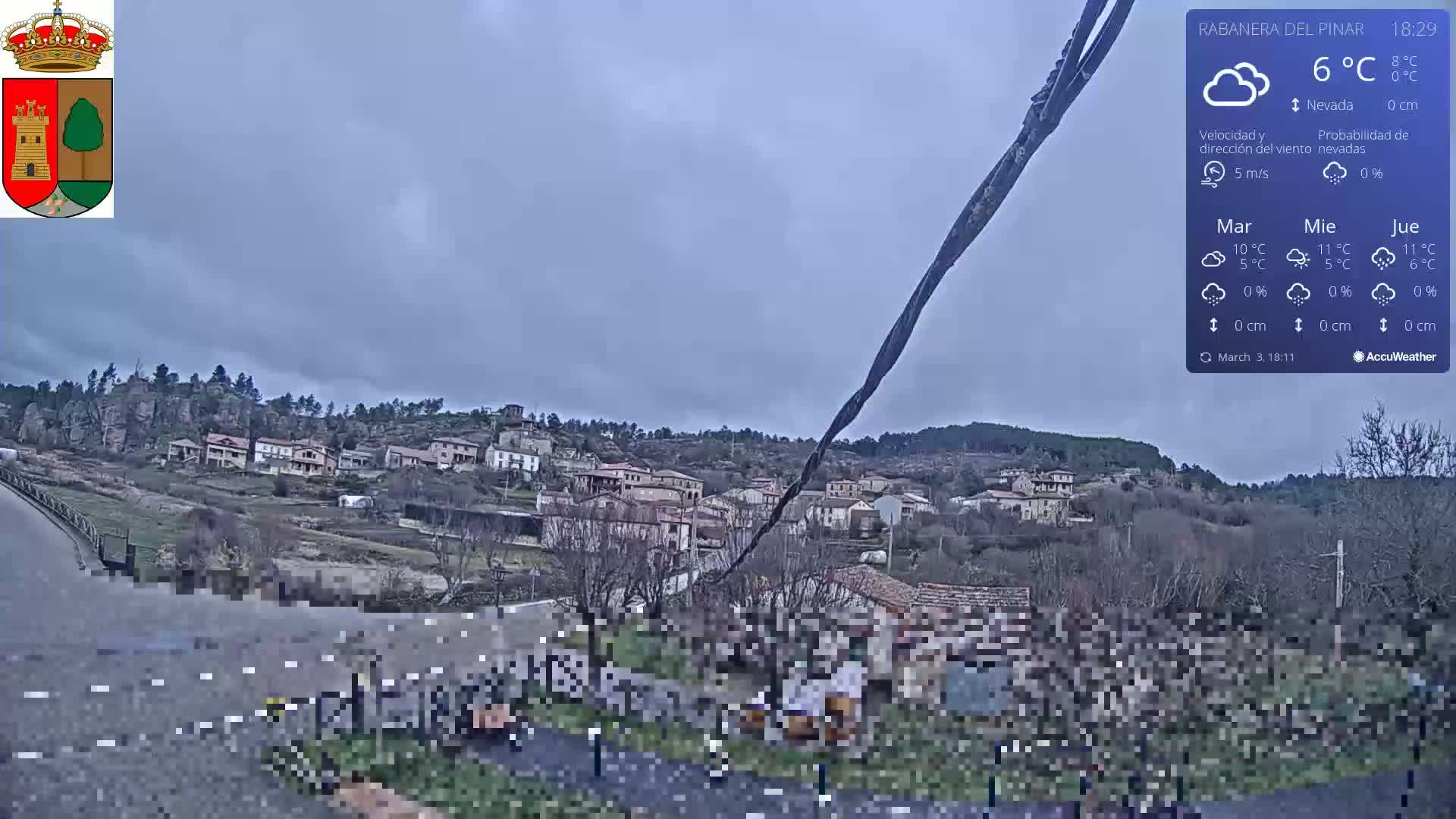 A small village nestled on a hillside under an overcast sky, with light snowfall.