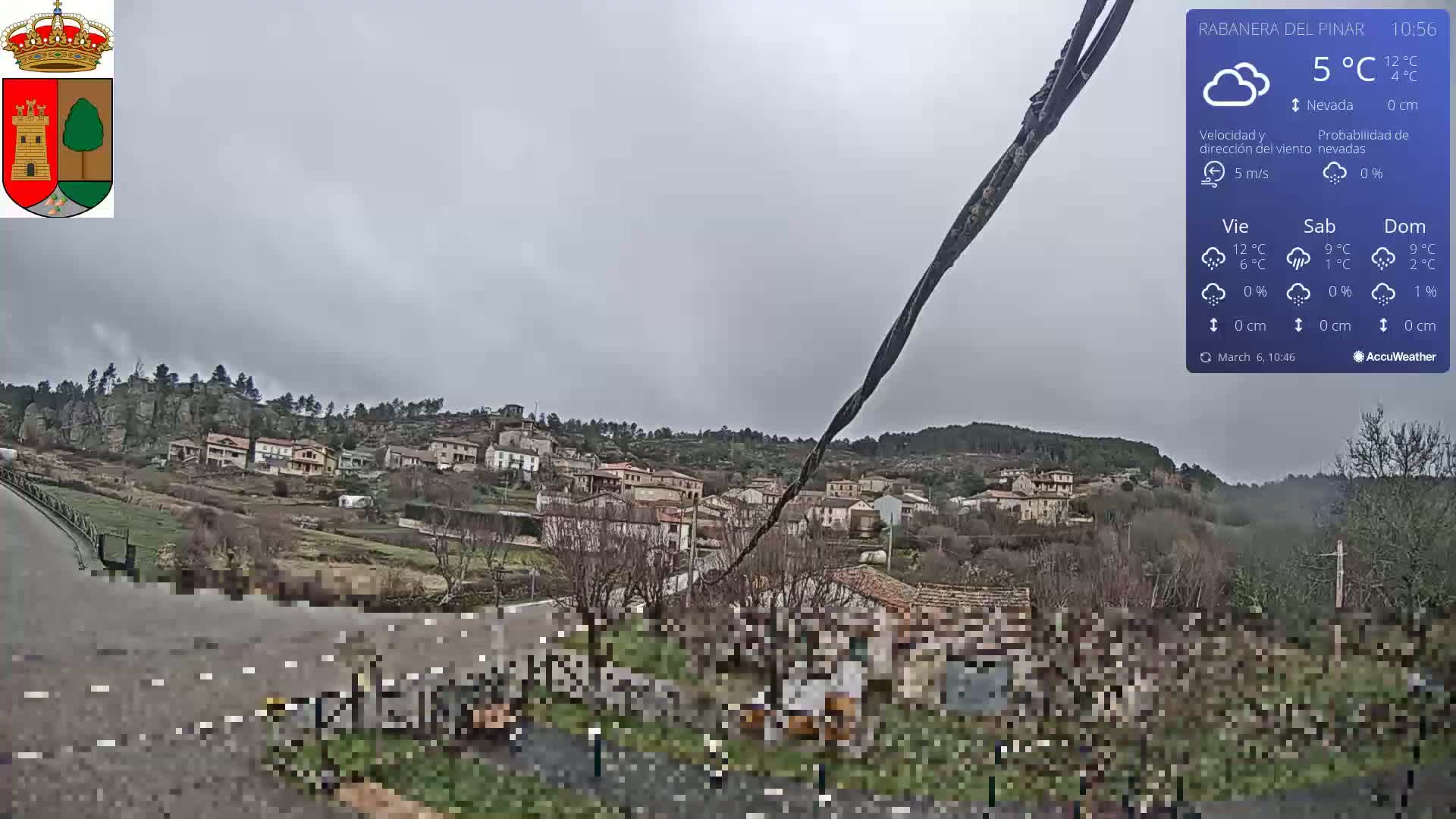 A small village nestled on a hillside under an overcast sky is seen from a slightly elevated vantage point.