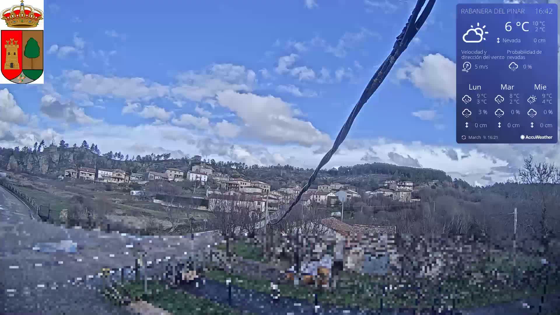 A partly cloudy day reveals a small village nestled on a hillside, with a few people gathered near the bottom of the hill.