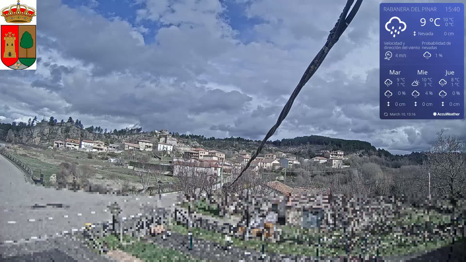 A small village nestled on a hillside under a partly cloudy sky is viewed from a roadside vantage point.