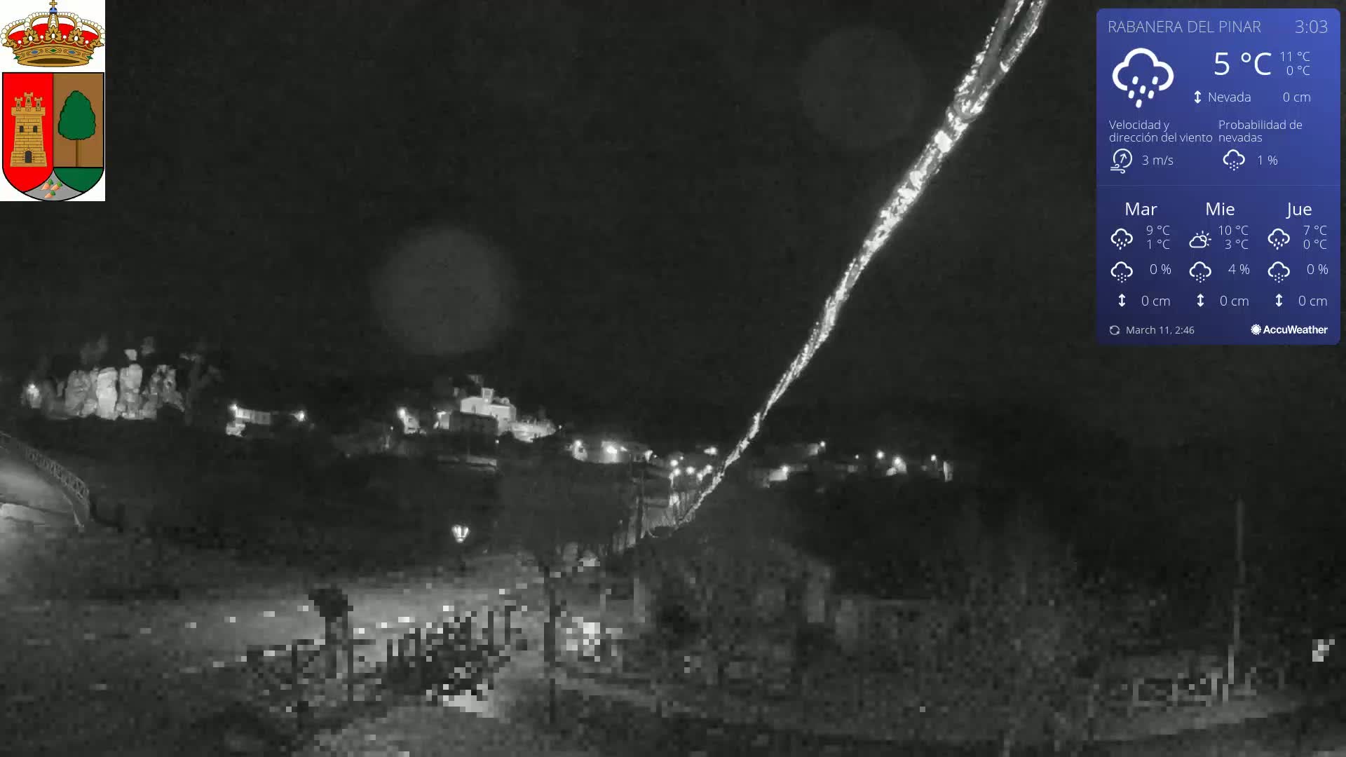 A nighttime, low-light view of a town illuminated by scattered lights under a slightly snowy, overcast sky.
