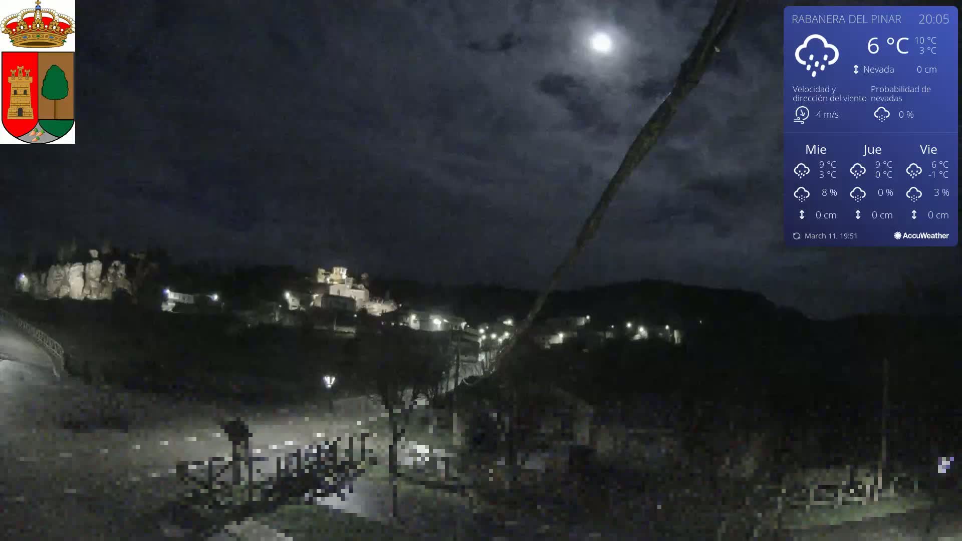 A nighttime view of a small town nestled in a valley under a partly cloudy sky with a bright moon.