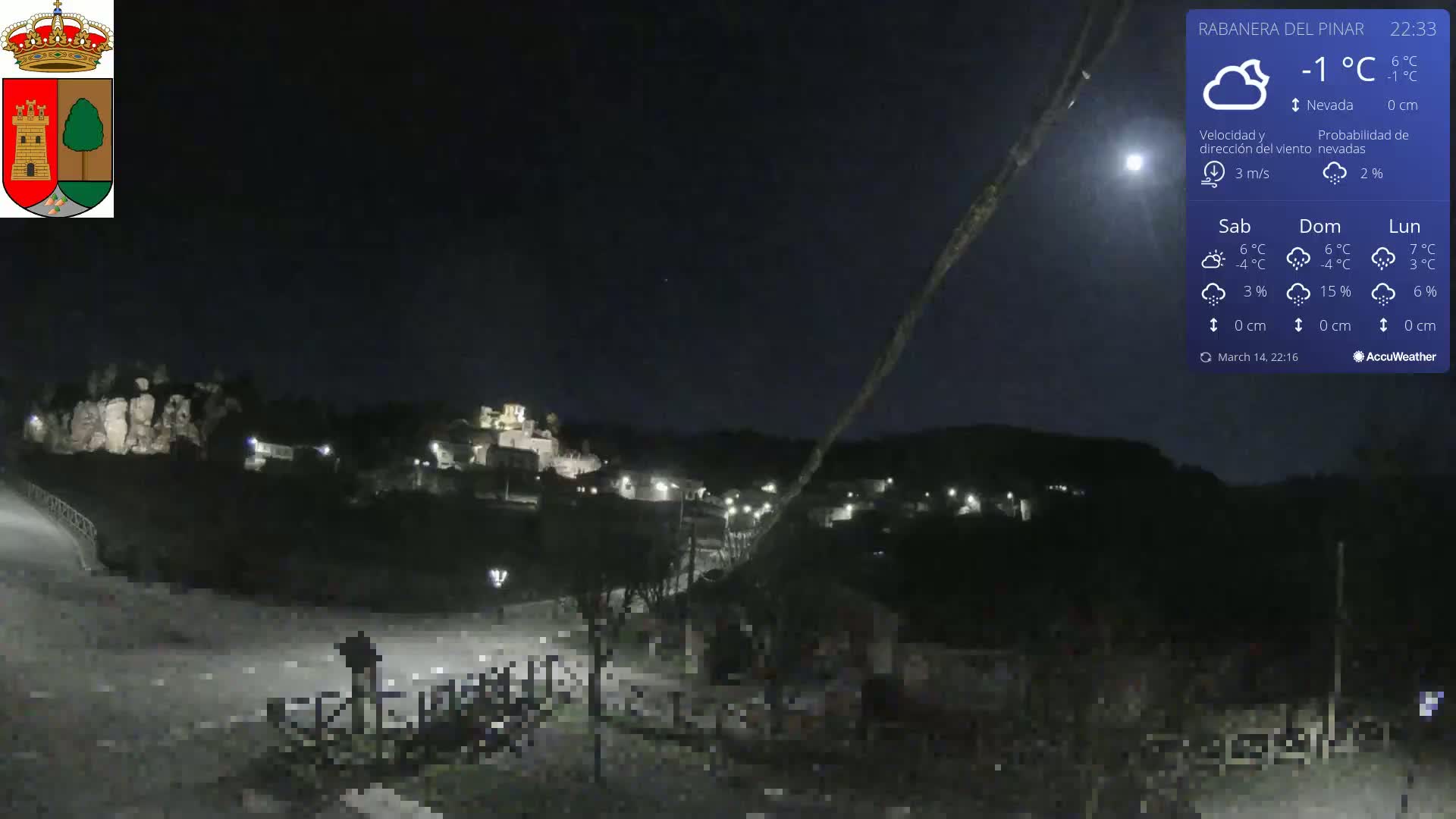 A nighttime view of a small town nestled in a hilly landscape under a clear, dark sky with a visible moon and a temperature of -1°C.