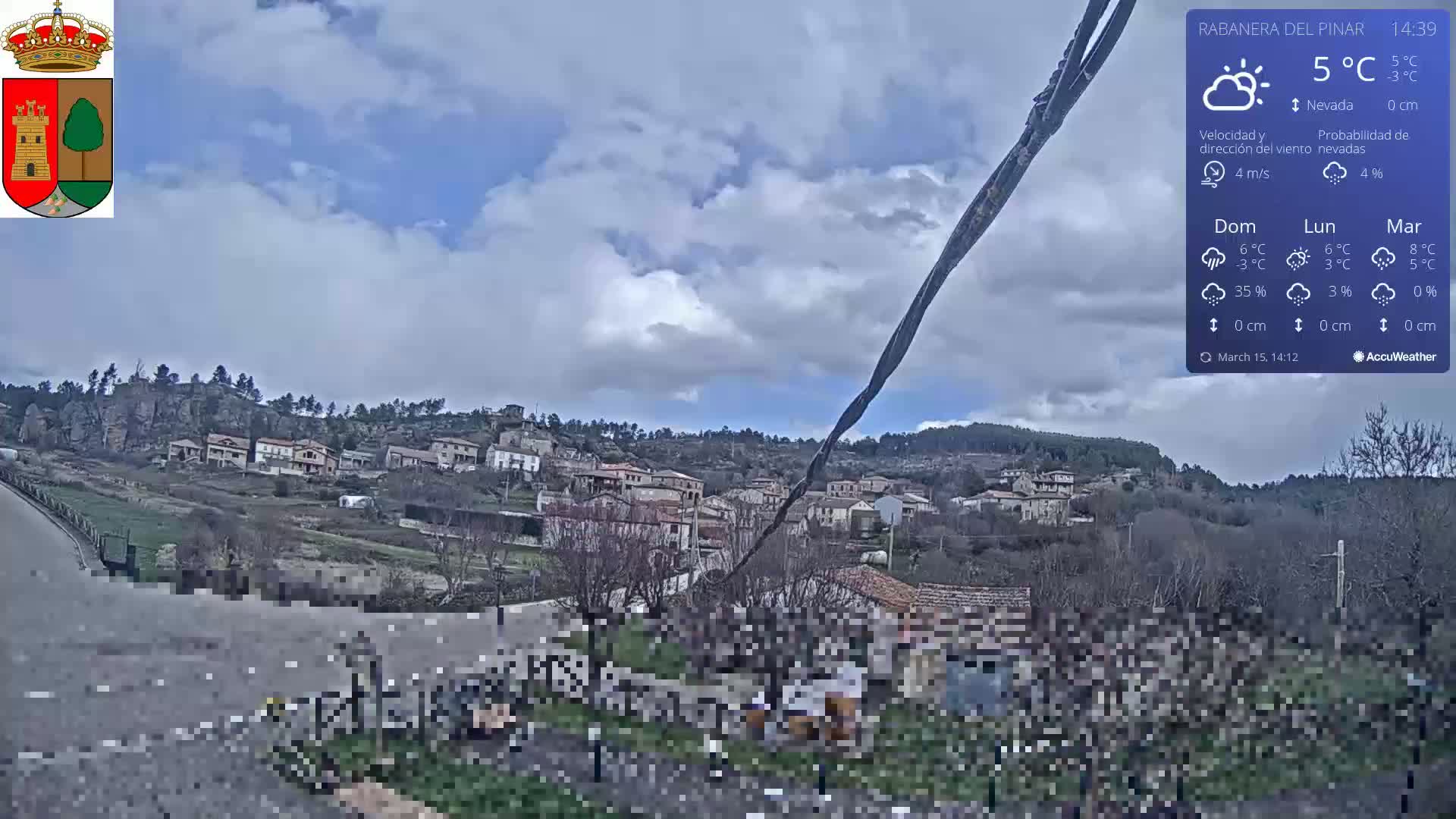 A partly cloudy day with a 5°C temperature shows a small town nestled on a hillside, viewed from a slightly elevated vantage point.