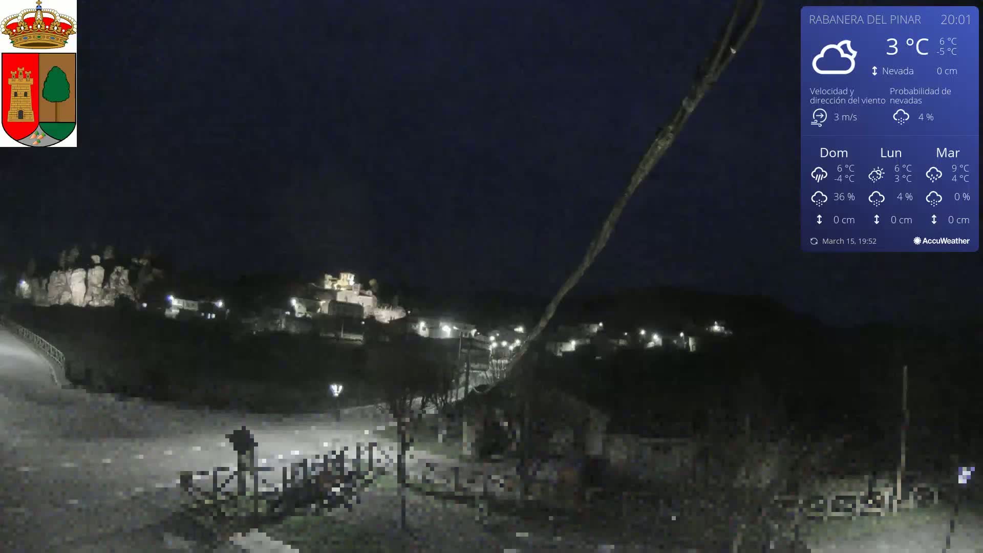 A nighttime view of a small, dimly lit town nestled in a hilly landscape under a clear, dark sky.