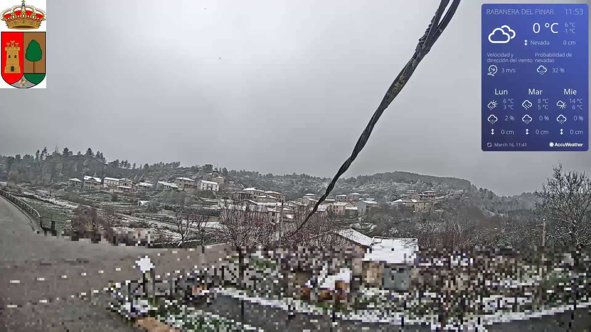 A snow-covered village is viewed from a slightly elevated position during a light snowfall.