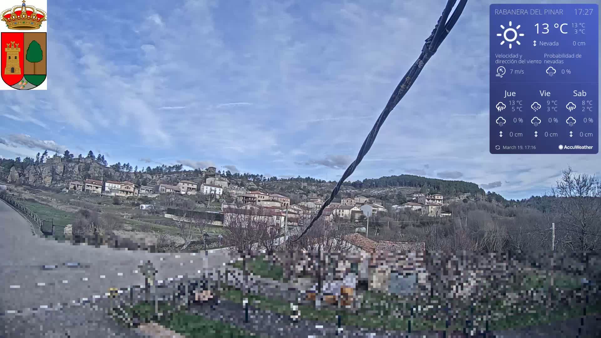 A small village nestled on a hillside under a mostly clear blue sky with a few wispy clouds.