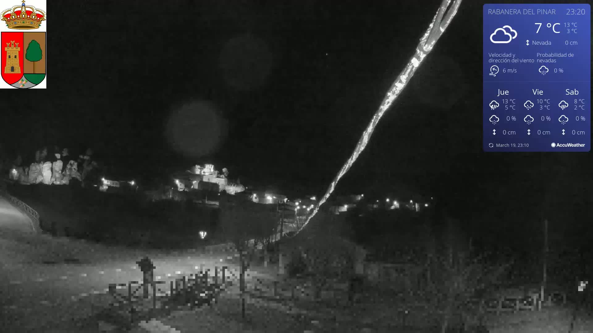 A nighttime, low-light view of a small town under a dark sky with a bright streak of light possibly from a meteor shower or similar phenomenon.