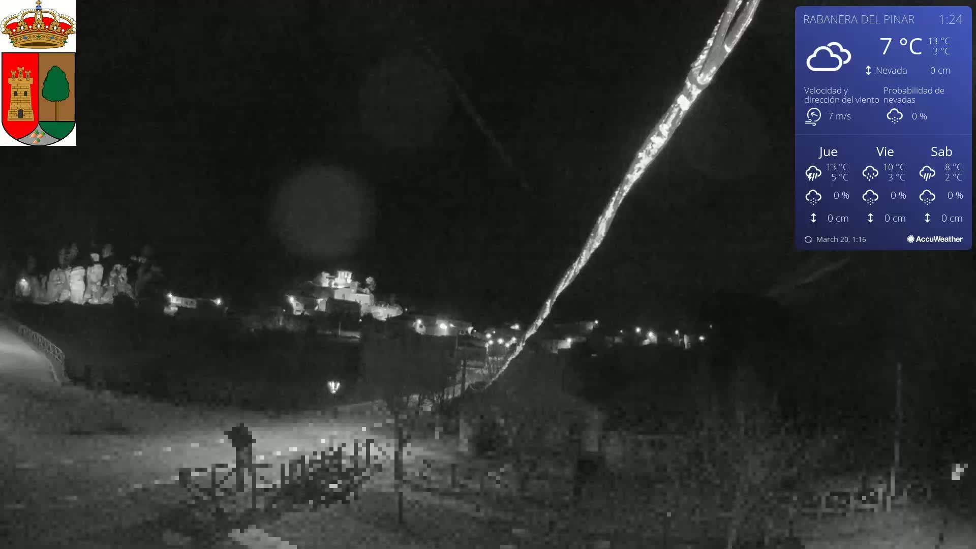 A nighttime, snowy scene shows a small town illuminated under a bright, nearly vertical streak of light in the sky.