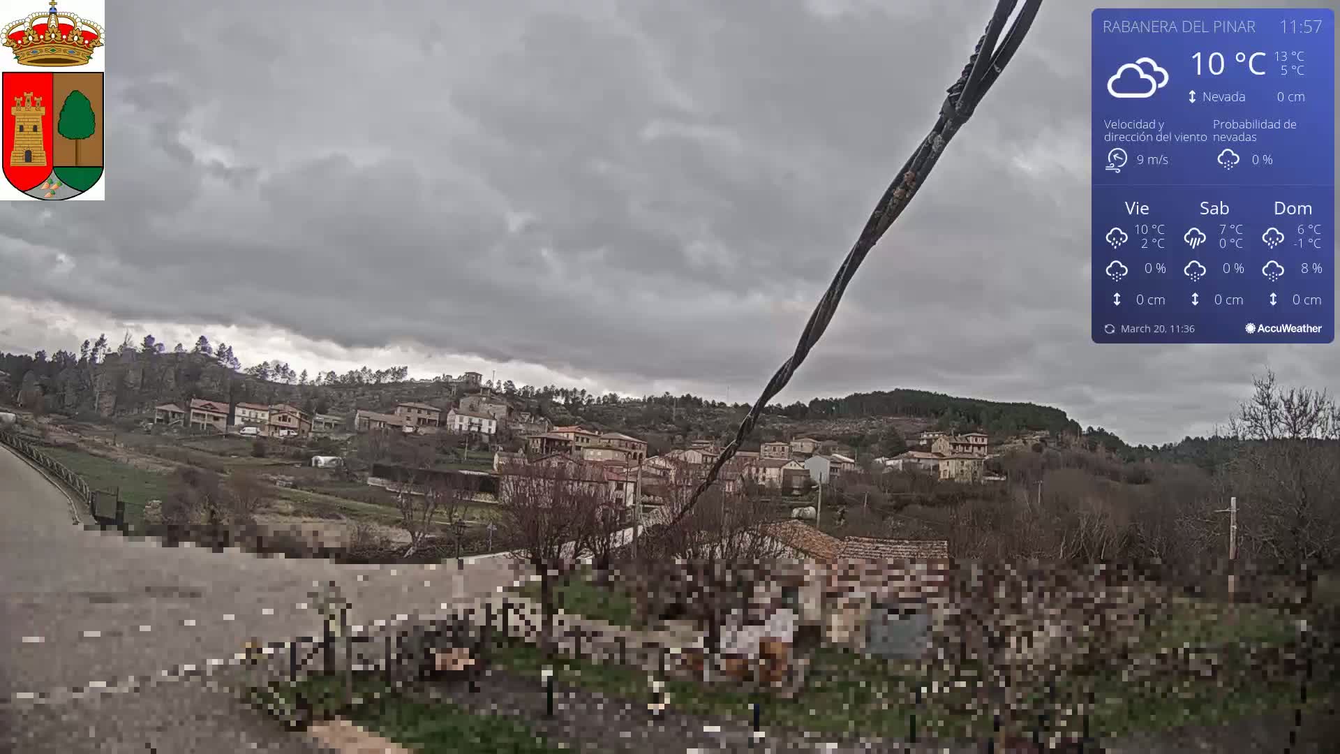 A small village nestled in a hillside is viewed from a roadside under an overcast sky.