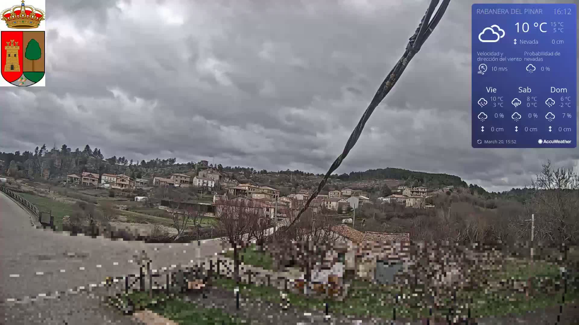 A small village nestled in a hillside under a cloudy, overcast sky is viewed from a slightly elevated vantage point.