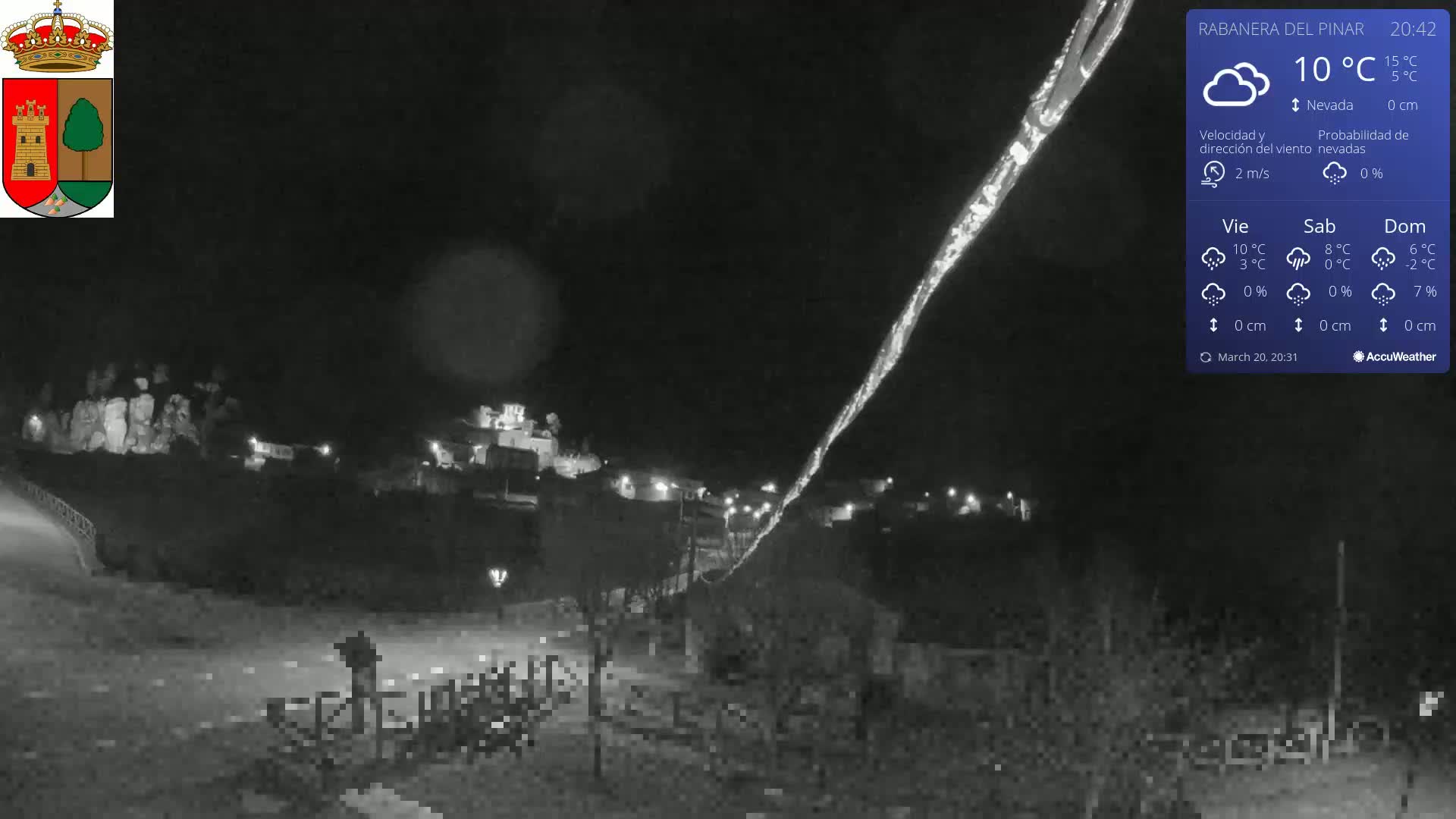 A nighttime, snowy scene shows a small town illuminated with faint lights under a dark sky, with a streak of bright light possibly from a meteor.