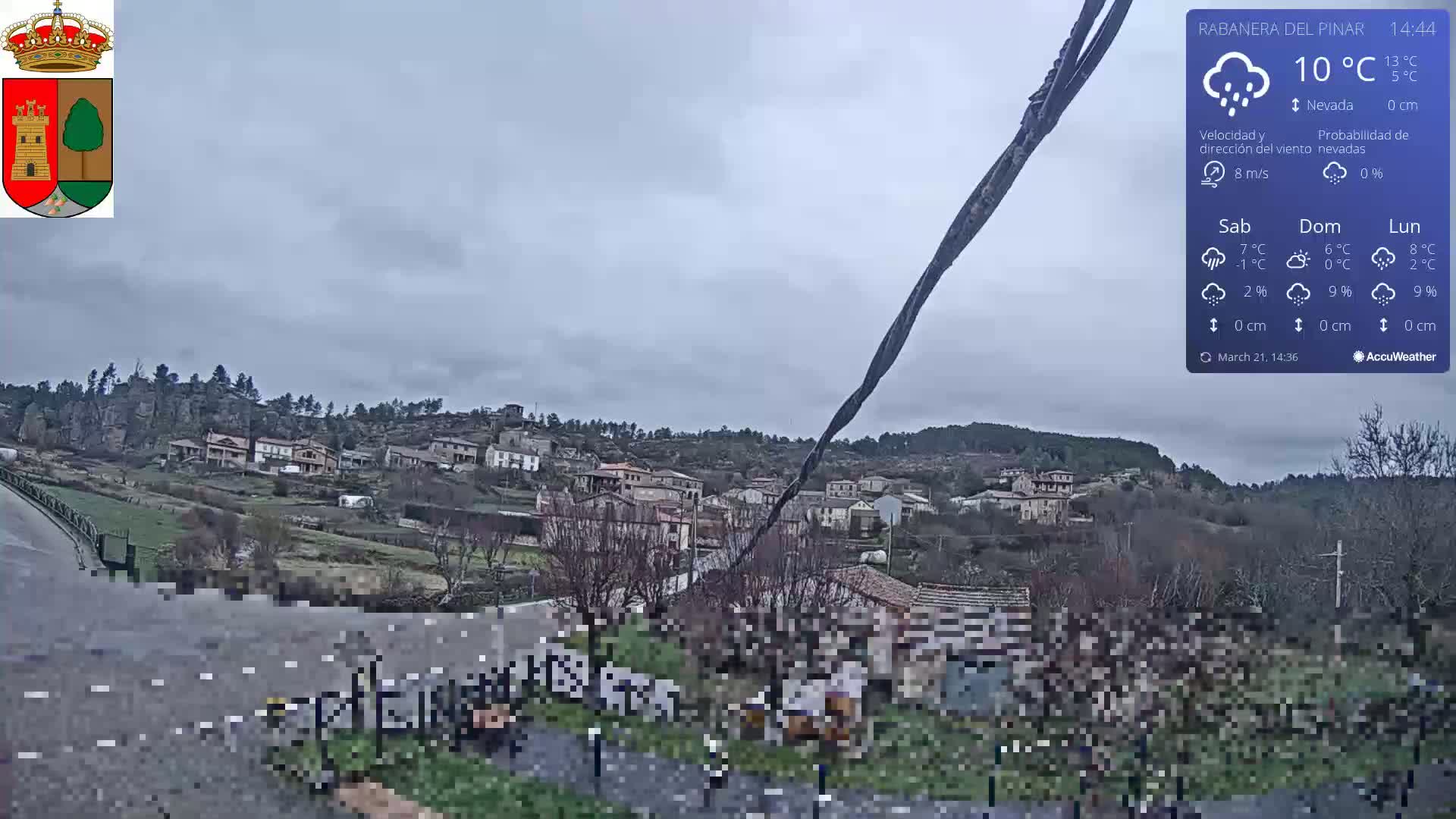 A small village nestled in a hillside is viewed on an overcast day with a light snowfall.