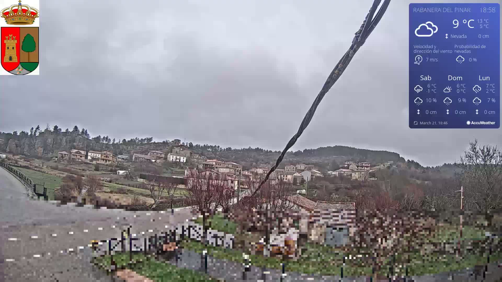 A small village nestled on a hillside under an overcast sky, with light snowfall possible.