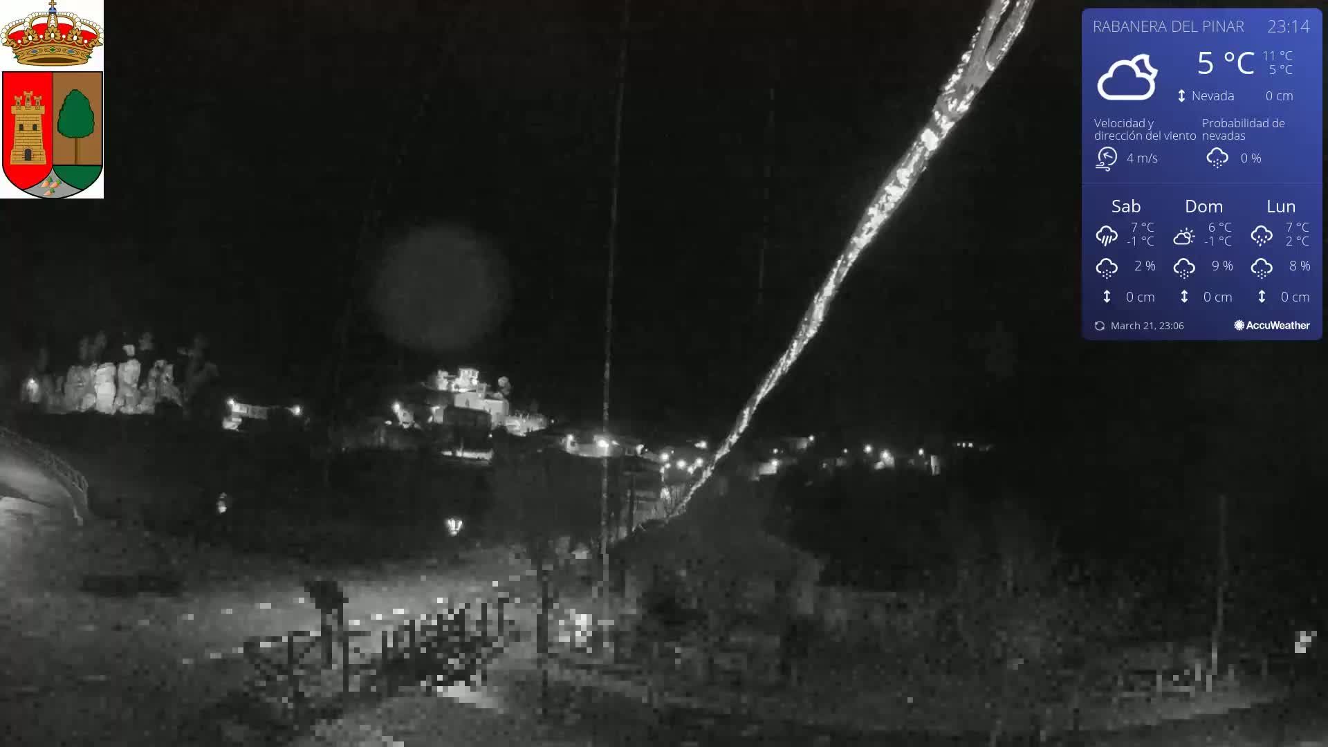 A nighttime, snowy scene shows a small town illuminated by scattered lights, with a faint, bright streak in the sky.
