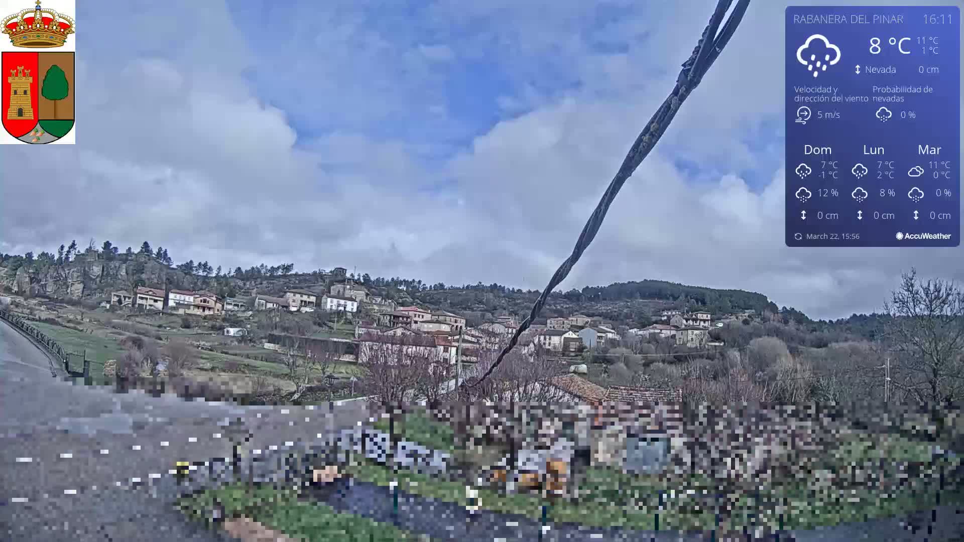 A small village nestled in a hillside is seen under a partly cloudy sky with a chance of snow.