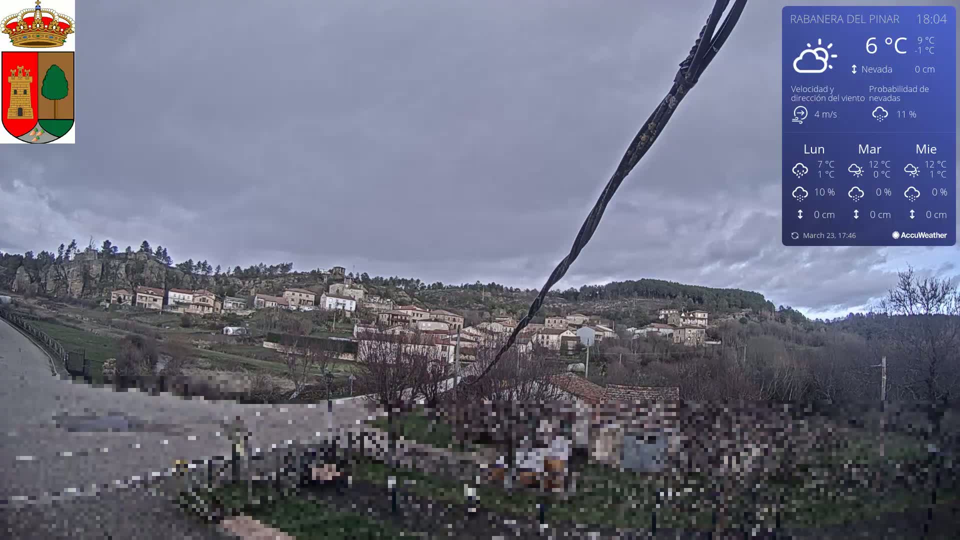 A small village nestled on a hillside under a cloudy, overcast sky is viewed from a slight distance.